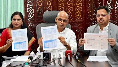 Three individuals seated at a table, holding papers and speaking into microphones during a formal event or press conference.