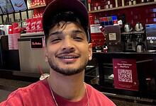 A young man smiling at a coffee shop counter with red and black decor.