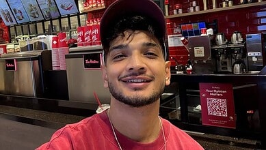 A young man smiling at a coffee shop counter with red and black decor.