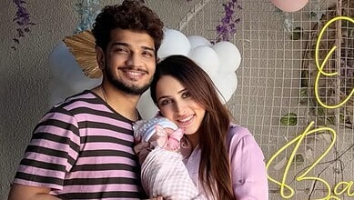 A newborn girl with her parents celebrating at a festive event, smiling and dressed in pink, with decorat.