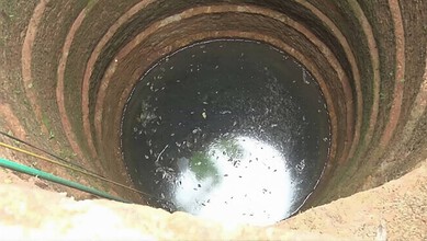A deep well with water at the bottom, surrounded by brick walls, in an outdoor setting.