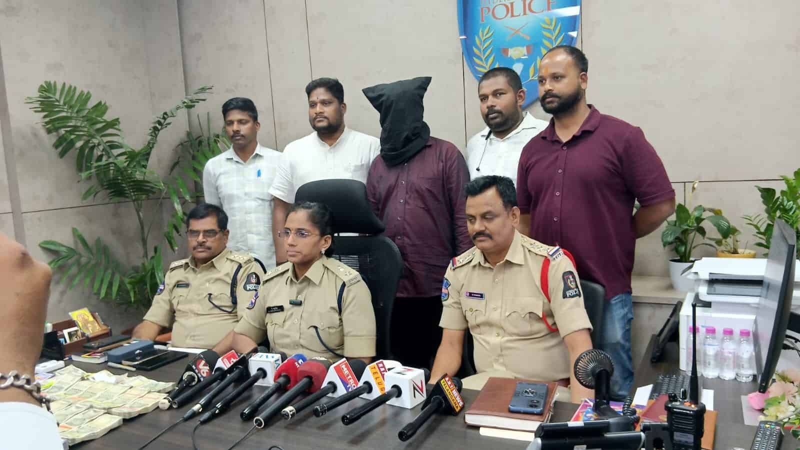 A police officer seated at a desk with five men standing behind, in a press conference setting.