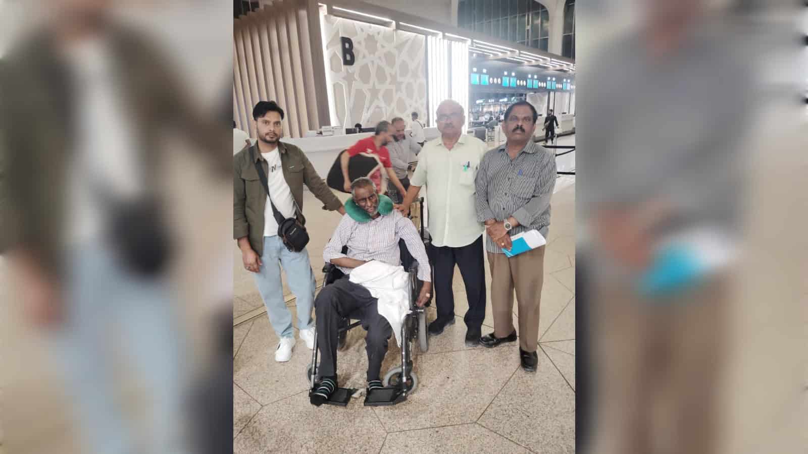 Indian man in wheelchair with family at airport, returning home after stroke treatment in Saudi Arabia.