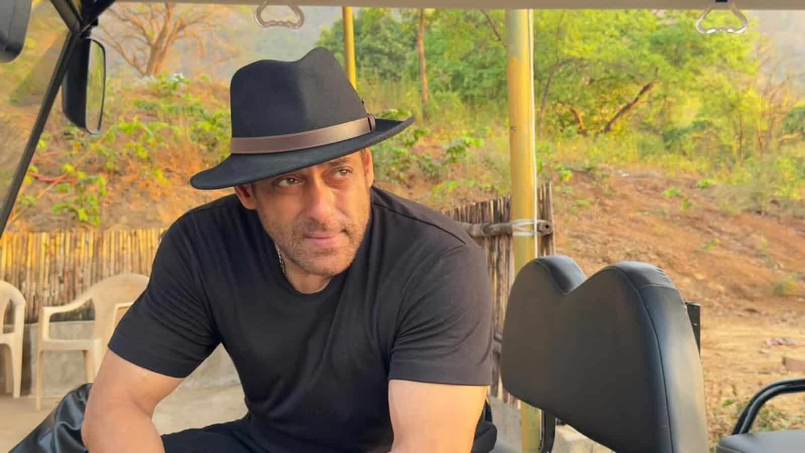 Salman Khan wearing a black hat and t-shirt outdoors, with greenery in the background.