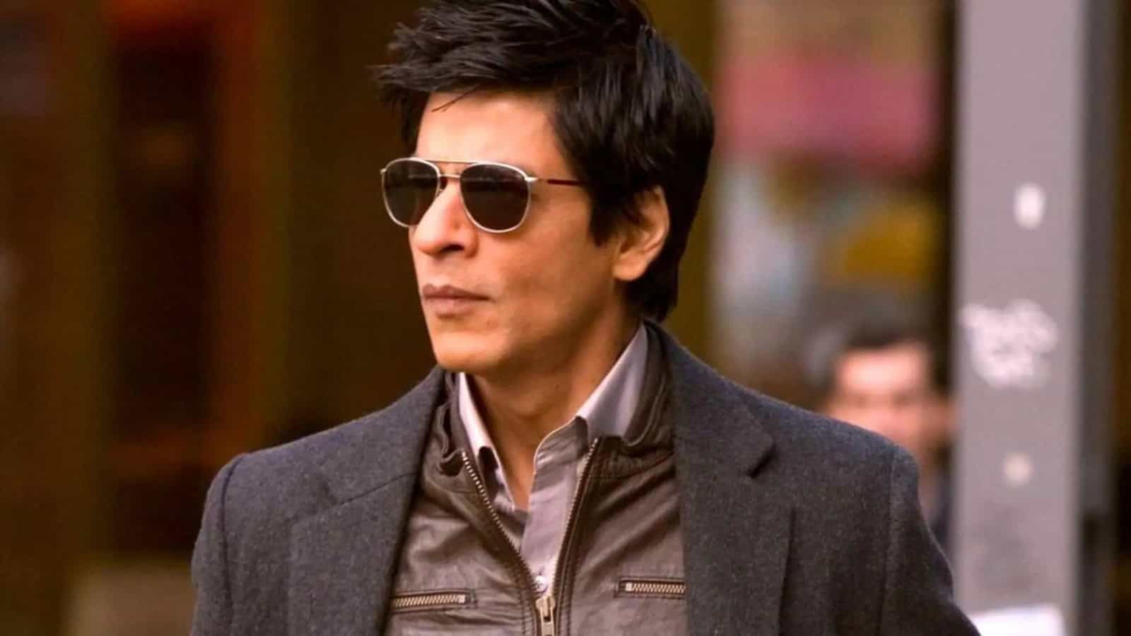 A woman with short dark hair wearing sunglasses and a grey blazer, standing outdoors in an urban setting.