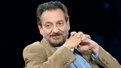 Shekhar Kapur seated with hands clasped, wearing a blazer against a dark background.