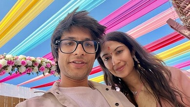 A young man and woman taking a selfie under colorful hanging decorations at a festive event.