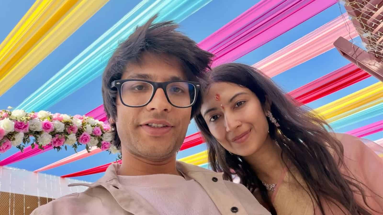A young man and woman taking a selfie under colorful hanging decorations at a festive event.