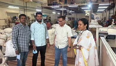 Manufacturing workers inspecting textiles in a busy factory setting, with fabric rolls and machinery in t.