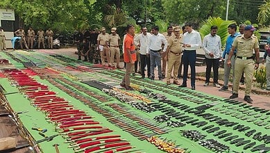 Police and officials inspecting seized weapons and ammunition displayed outdoors.