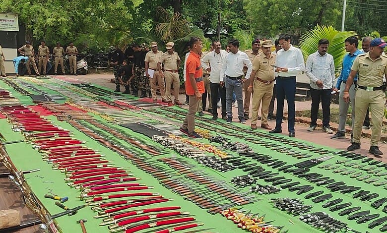 Police and officials inspecting seized weapons and ammunition displayed outdoors.