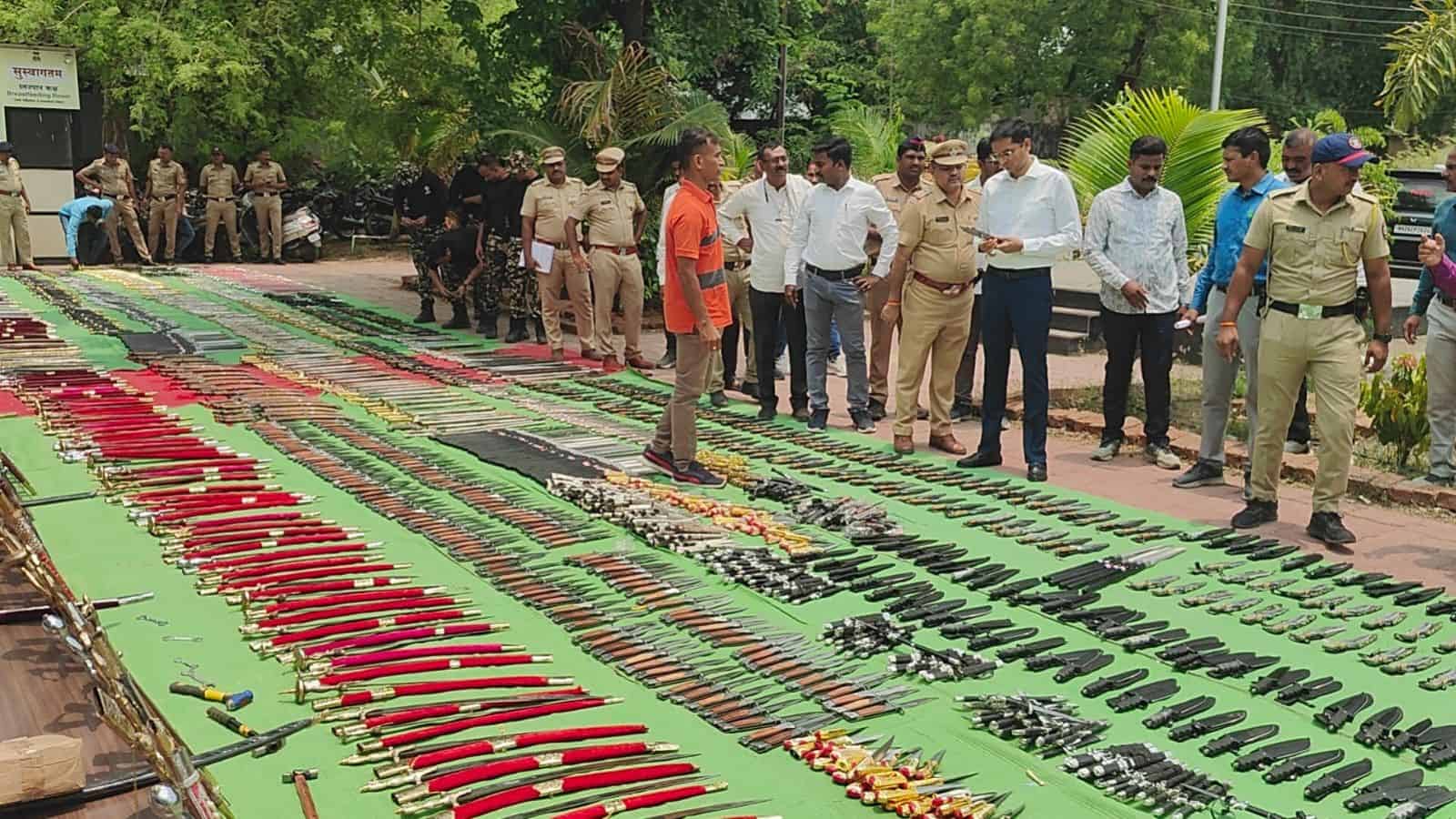 Police and officials inspecting seized weapons and ammunition displayed outdoors.