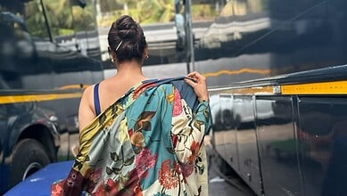 A woman in a colorful saree walking near parked vehicles in an urban setting.