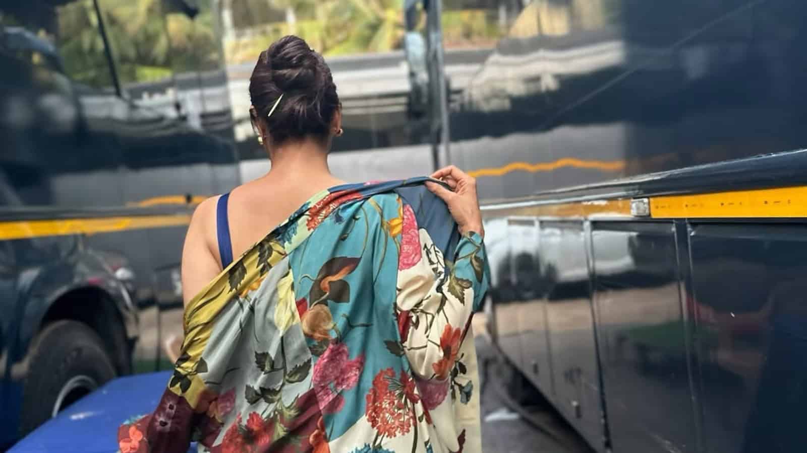 A woman in a colorful saree walking near parked vehicles in an urban setting.
