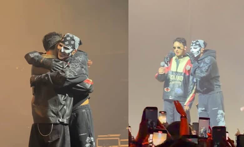 A woman and a man hugging on stage during a music event, with another performer speaking into a microphon.