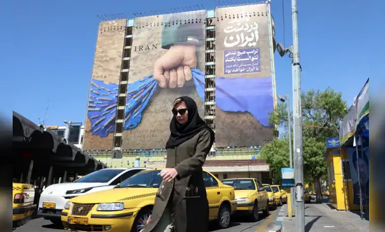 Protest against Iran's regime with a woman holding a blue rope in front of a large mural.