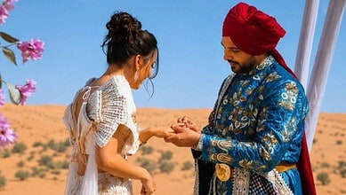 A young woman and a man in traditional Indian attire exchanging rings outdoors in a desert landscape.