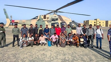 Group of men and women standing beside a military helicopter on an open field in daytime.