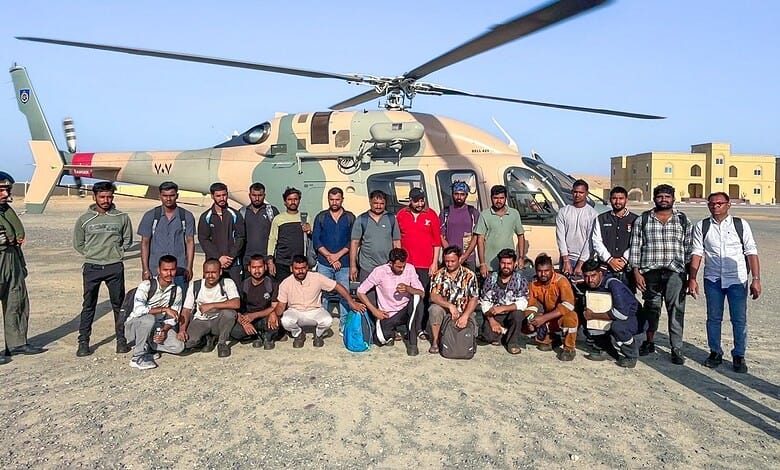 Group of men and women standing beside a military helicopter on an open field in daytime.