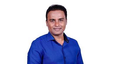 A smiling man in a blue shirt posing for a professional photo for The Siasat Daily.