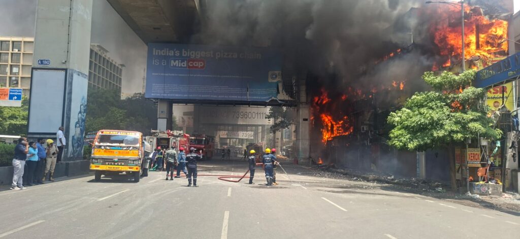 Fire outbreak at a commercial building in a busy city street, with emergency responders present.