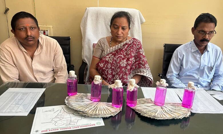 A woman and two men seated at a table with bottles of pink liquid and documents, in an indoor setting.