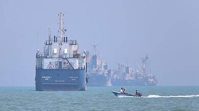 Large cargo ships and a speedboat on the sea, with a hazy horizon and distant ships.