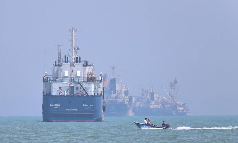 Large cargo ships and a speedboat on the sea, with a hazy horizon and distant ships.