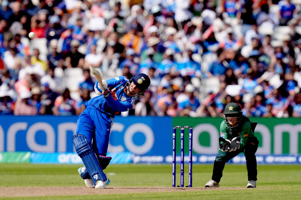 A cricket player in blue uniform batting during a match with a crowd in the background.