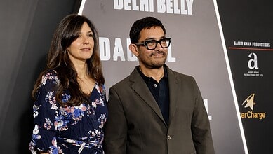 A woman and a man standing together at a promotional event for Delhi Belly, with a backdrop featuring the.