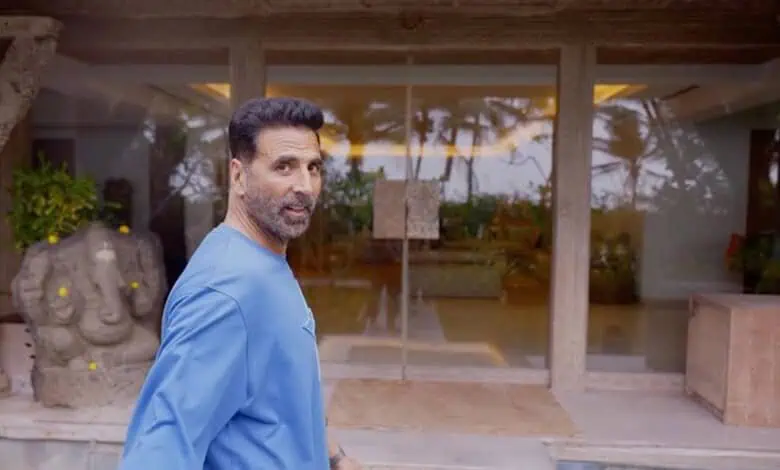Man in blue shirt standing outdoors near a modern building with glass doors and tropical plants.