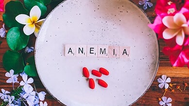 A plate with the word Amenia spelled out with letter tiles and red pills, surrounded by colorful flowers.
