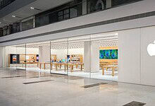 Apple Store interior with wooden tables displaying products and a large colourful artwork on the wall.