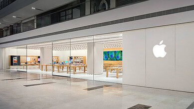 Apple Store interior with wooden tables displaying products and a large colourful artwork on the wall.