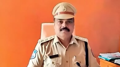 A police officer in uniform sitting at a desk with files and papers against an orange background.