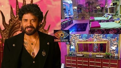 A woman with curly hair and a beard, wearing a black jacket, smiling in front of a pink background with d.