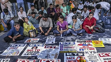 Protesters sit on the ground at Jantar Mantar holding signs against paper leaks and scams.