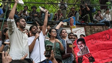 Protesters holding signs and banners during a public demonstration in an outdoor setting with trees.