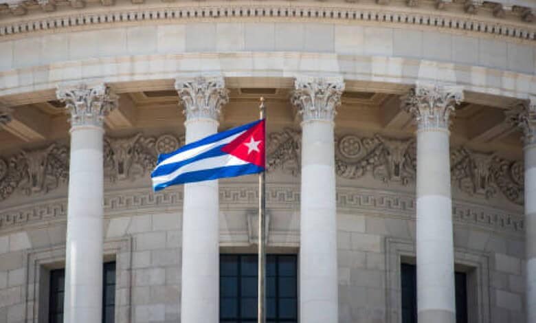 Cuban flag waving in front of a government building with classical columns and ornate architecture.