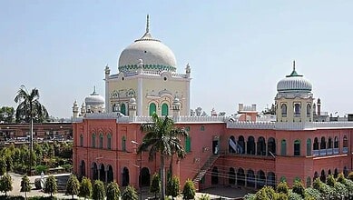 Colourful mosque with domes and minarets, surrounded by lush greenery and palm trees, under a clear blue.