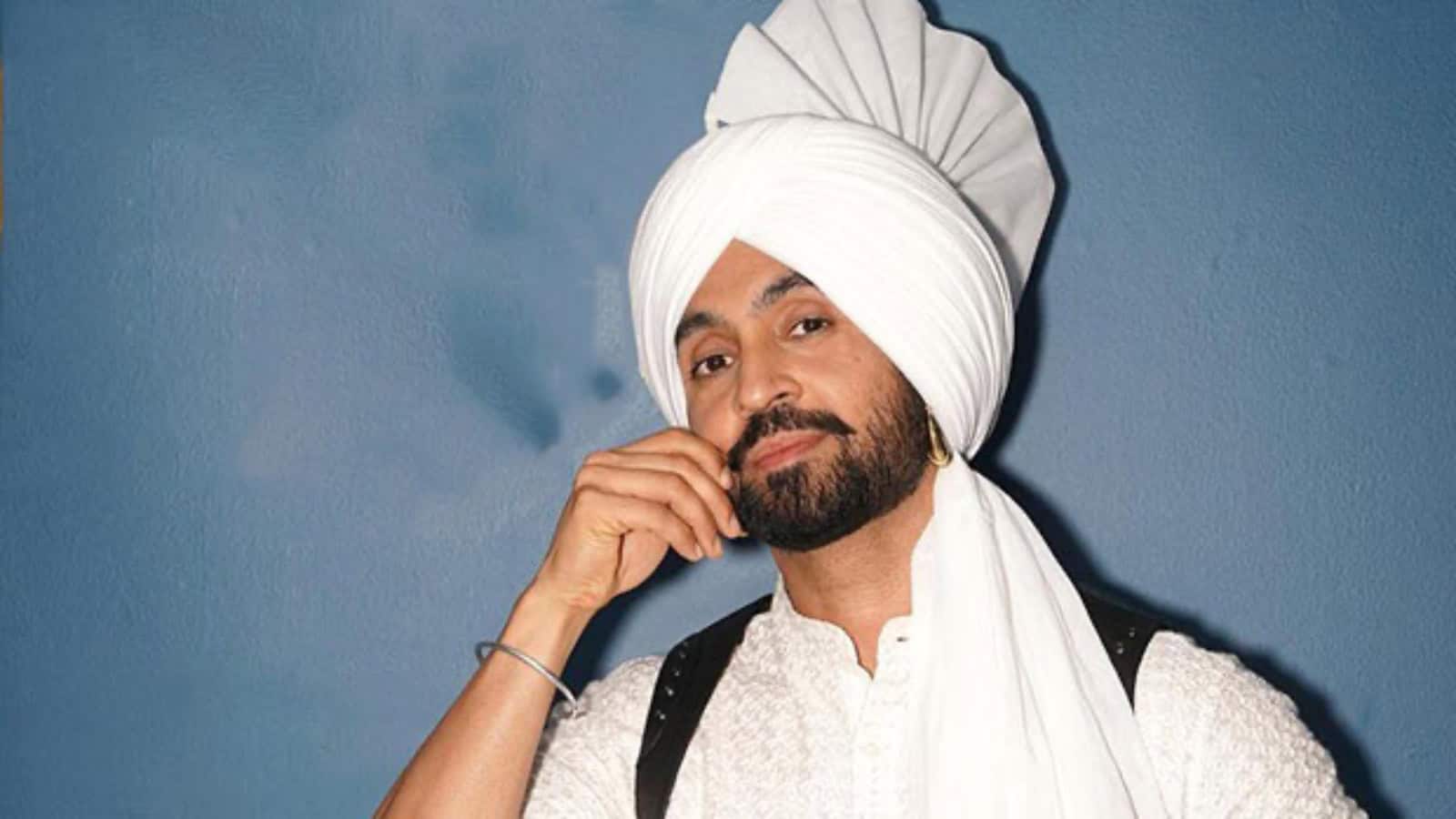 A traditional Sikh man wearing a white turban and beard, posing confidently against a blue background.