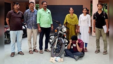 A man working on a motorcycle surrounded by five people, including women in traditional attire, in an out.