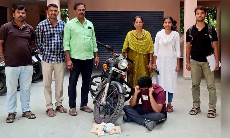 A man working on a motorcycle surrounded by five people, including women in traditional attire, in an out.