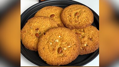 Close-up of golden, crispy dum-ke-roat cookies with nuts on a black plate.