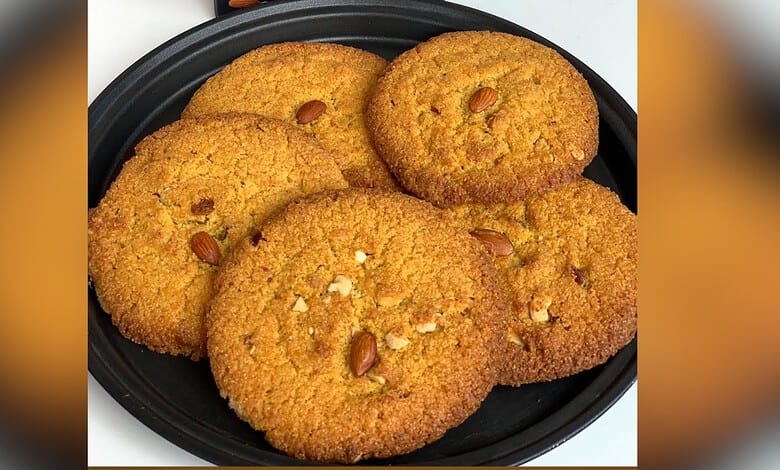 Close-up of golden, crispy dum-ke-roat cookies with nuts on a black plate.