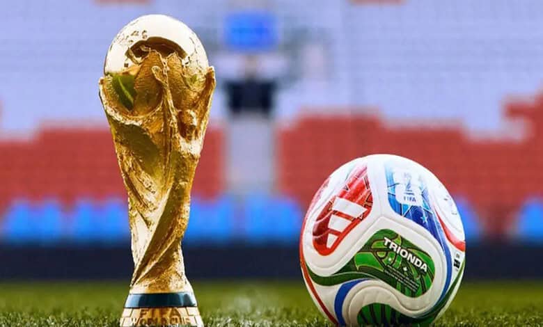Golden FIFA World Cup trophy and a colourful football on a stadium pitch.