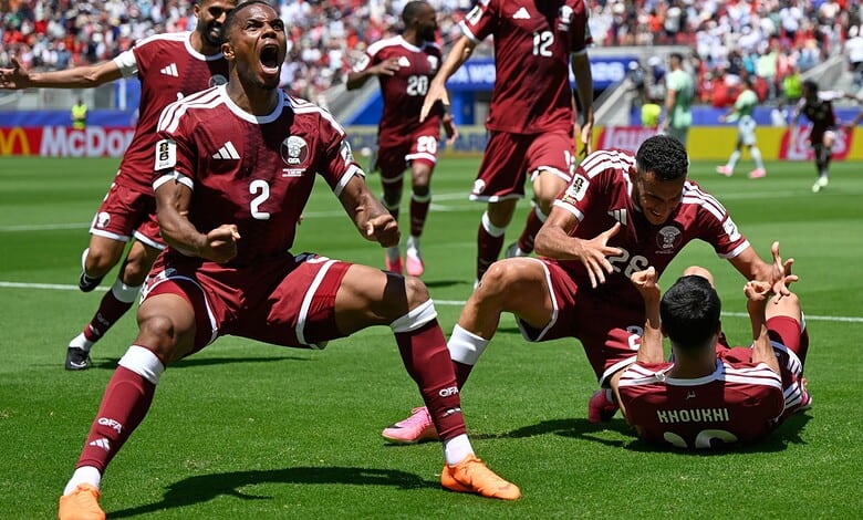 Celebrating a goal, Qatar football team players in maroon jerseys on the field during a match.