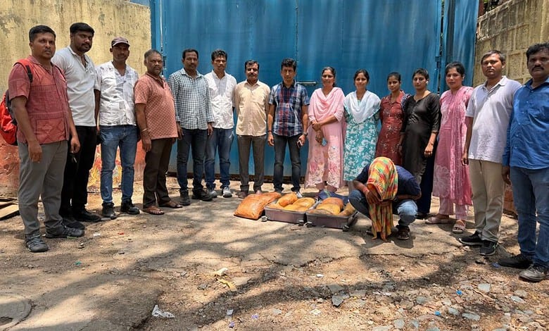 Group of people standing outdoors with a woman kneeling on the ground in front of bags of food.
