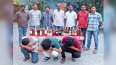 A group of seven men standing behind a table with various bottles of alcohol, three men kneeling in front.