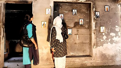 A woman viewing framed photographs displayed on a weathered wall in an indoor setting.